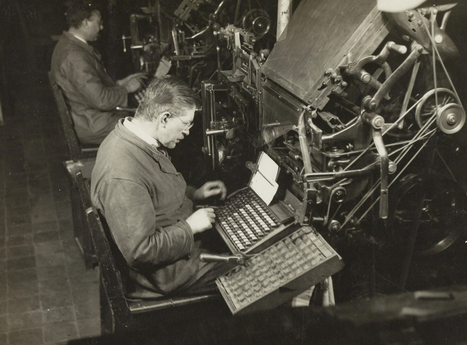 Vintage photograph of a Linotype operator at his keyboard, a person directing a complex typesetting machine to do the heavy mechanical work.
